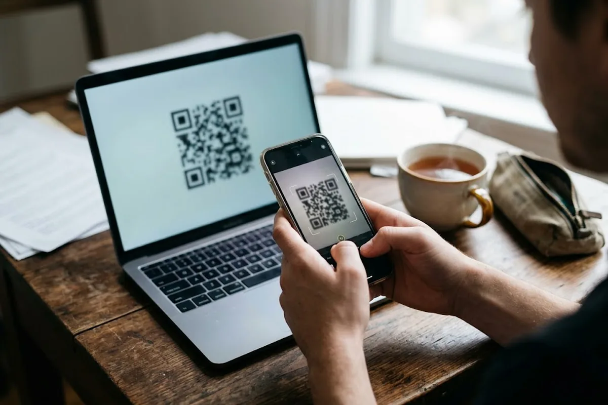 Человек сканирует QR-код для установки eSIM с экрана ноутбука смартфоном